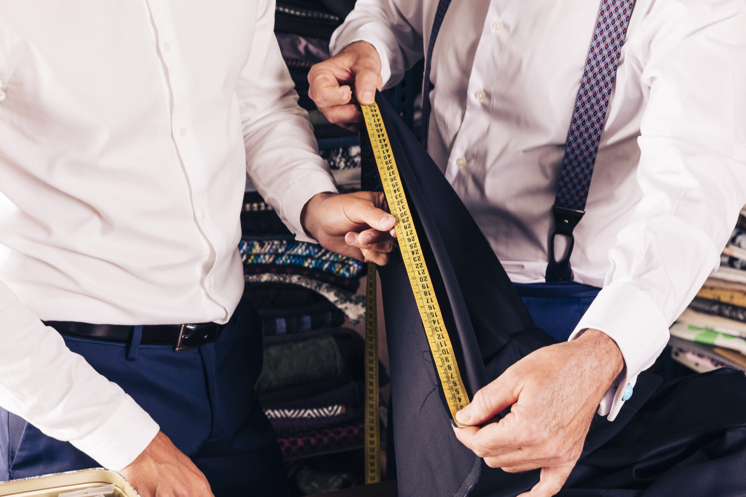 customer-senior-male-tailor-measuring-fabric-with-yellow-measure-table